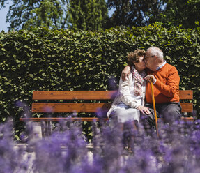Senior couple sitting on bench in a park, kissing - UUF14938