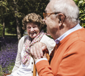 Senior couple sitting on bench in a park, talking - UUF14940