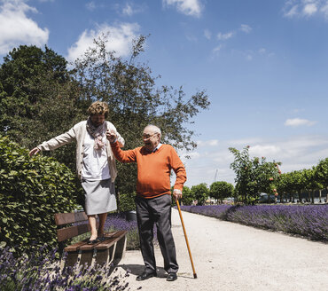 Älteres Paar, das sich im Park amüsiert, älterer Mann, der einer Frau hilft, auf einer Bank zu balancieren - UUF14943