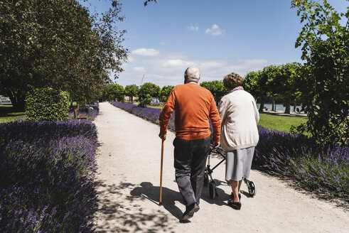 Älteres Paar geht im Park spazieren, die Frau benutzt eine Gehhilfe auf Rädern - UUF14947