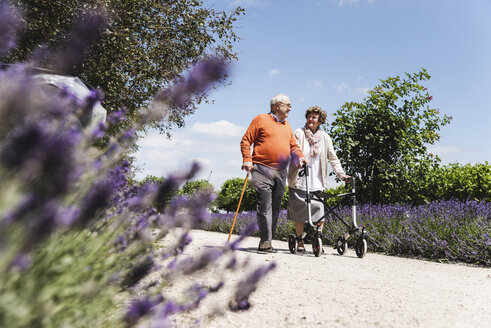 Älteres Paar geht im Park spazieren, die Frau benutzt eine Gehhilfe auf Rädern - UUF14948