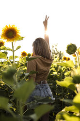 Junge Frau steht in einem Sonnenblumenfeld und macht ein Siegeszeichen - ACPF00295