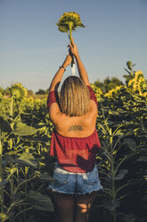 Junge Frau steht auf einem Feld und hebt eine Sonnenblume - ACPF00297