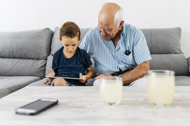 Großvater und Enkel sitzen zusammen auf der Couch zu Hause und schauen auf ein digitales Tablet - JRFF01798