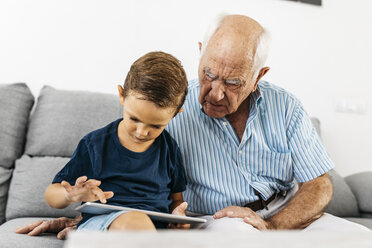 Grandfather and grandson sitting together on the couch at home using digital tablet - JRFF01799