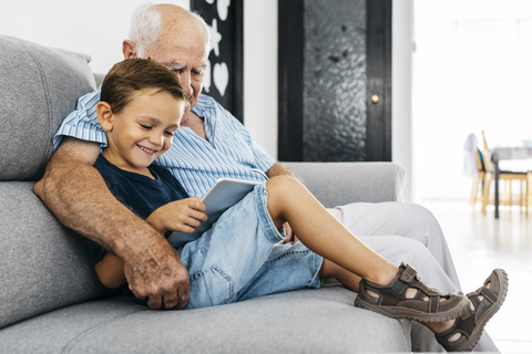 Großvater und Enkel sitzen zusammen auf der Couch zu Hause und schauen auf ein digitales Tablet, lizenzfreies Stockfoto