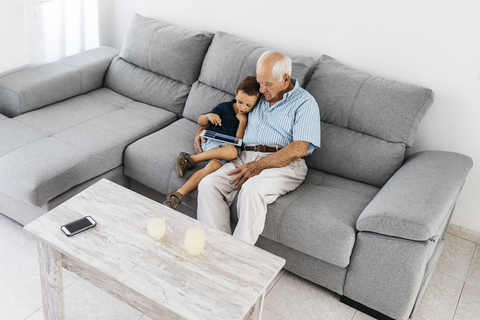 Großvater und Enkel sitzen zusammen auf der Couch zu Hause und schauen auf ein digitales Tablet, lizenzfreies Stockfoto