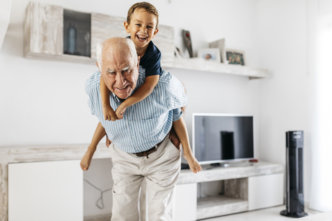 Porträt eines Großvaters, der seinen Enkel im Wohnzimmer Huckepack nimmt, lizenzfreies Stockfoto