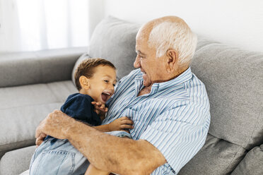 Grandson and grandfather laughing while tickling each other on the couch - JRFF01825