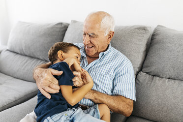 Grandson and grandfather laughing while tickling each other on the couch - JRFF01826
