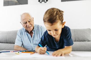 Portrait of smiling grandfather watching his grandson drawing with coloured pencils - JRFF01829