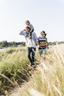 Glückliche Familie bei einem Spaziergang am Flussufer an einem schönen Sommertag - UUF14978