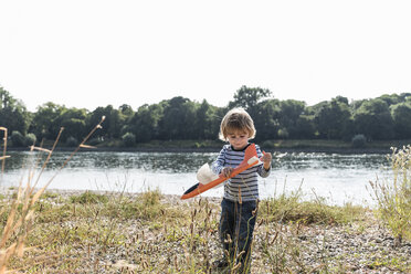 Junge spielt mit einem Spielzeugflugzeug am Flussufer - UUF14990