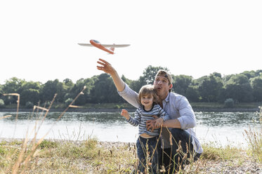 Vater und Sohn haben Spaß am Flussufer und spielen mit einem Spielzeugflugzeug - UUF14992