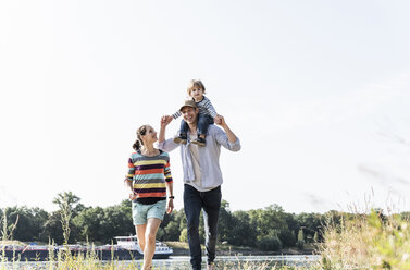 Glückliche Familie bei einem Spaziergang am Flussufer an einem schönen Sommertag - UUF14994