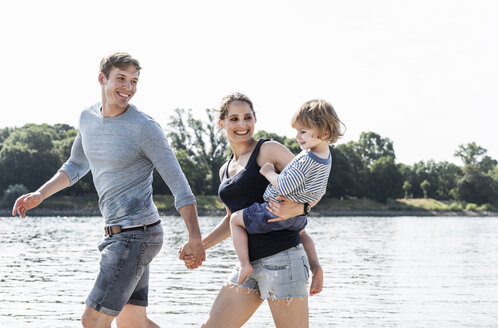 Glückliche Familie bei einem Spaziergang am Flussufer an einem schönen Sommertag - UUF15012