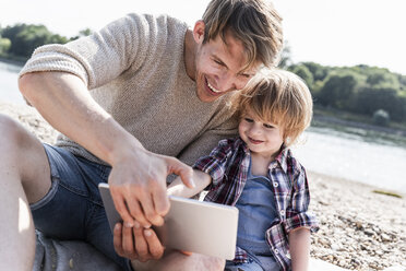 Father and son playing on digital tablet at the riverside - UUF15021