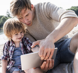 Vater und Sohn spielen am Flussufer auf einem digitalen Tablet - UUF15022