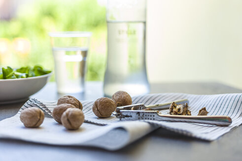 Whole and cracked walnuts and nutcracker on cloth on garden table - RAMAF00002