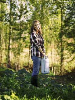 Portrait of smiling farmer with watering can on a field - RAMAF00052