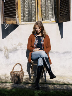 Porträt einer lächelnden Frau, die vor einem Haus sitzt und das Sonnenlicht genießt - RAMAF00053