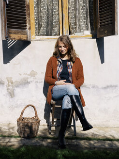 Portrait of smiling woman sitting in front of house enjoying sunlight - RAMAF00053