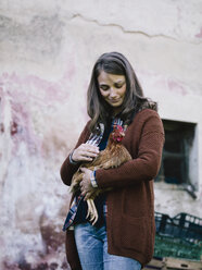 Smiling woman holding chicken on her arm - RAMAF00064