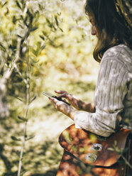 Italien, Frau lehnt an einem Olivenbaum und benutzt ein Mobiltelefon - RAMAF00071