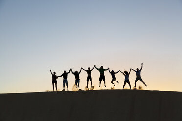 Fuerteventura, Naturpark Las Dunas (Corralejo), Silhouette einer Gruppe von Menschen, die auf einer großen Sanddüne springen - AURF02440