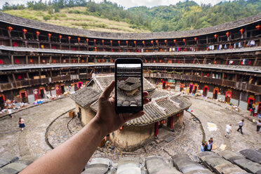 China, Provinz Fujian, Hand, die mit dem Handy den Innenhof eines Tulou in einem Hakka-Dorf fotografiert - KKAF01494