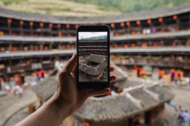 China, Provinz Fujian, Hand, die mit dem Handy den Innenhof eines Tulou in einem Hakka-Dorf fotografiert - KKAF01495