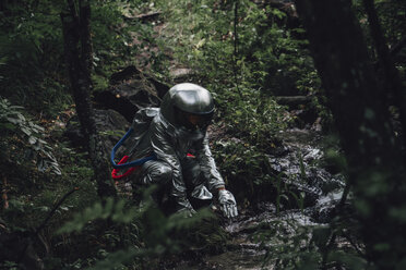 Spaceman exploring nature, crouching at a brook in forest - VPIF00543