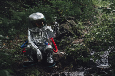 Spaceman exploring nature, crouching at a brook in forest - VPIF00545