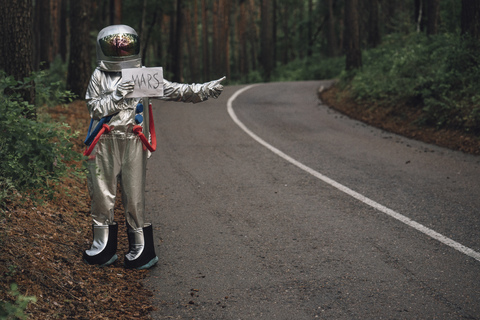 Raumfahrer, der per Anhalter zum Mars fährt, steht auf einer Straße im Wald, lizenzfreies Stockfoto