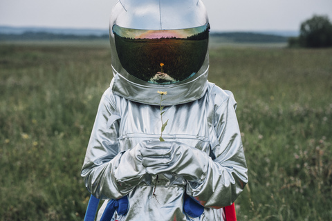 Raumfahrer hält Blume und sieht ihr beim Wachsen zu, lizenzfreies Stockfoto