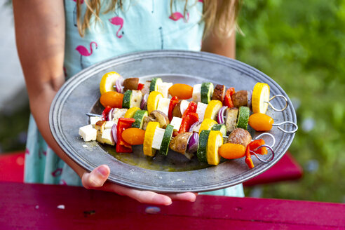 Mädchen mit Teller mit vegetarischen Grillspießen, Tomaten, gelben und grünen Zucchini, Tofu, Feta, Zwiebeln und Champignon - SARF03931