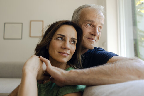 Smiling mature couple sitting on couch at home - KNSF04603