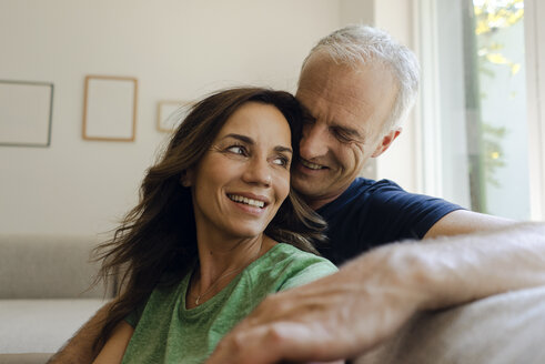 Smiling mature couple sitting on couch at home - KNSF04604