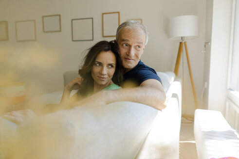 Smiling mature couple sitting on couch at home - KNSF04605
