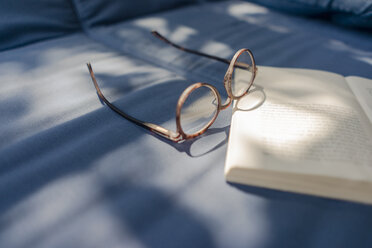 Eyeglasses and book lying on couch - KNSF04628