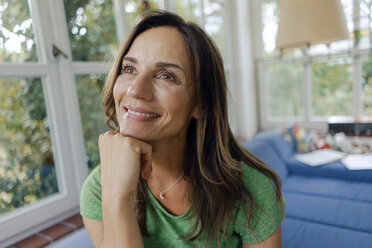 Smiling mature woman on couch at home looking away - KNSF04641