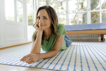 Porrait of smiling mature woman lying on the floor at home - KNSF04656