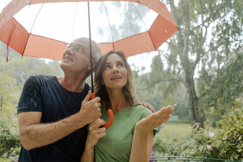 Smiling mature couple standing in rain under umbrella - KNSF04660