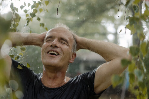 Smiling mature man enjoying summer rain in garden - KNSF04670