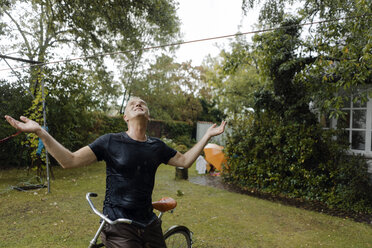 Mature man with bicycle enjoying summer rain in garden - KNSF04672