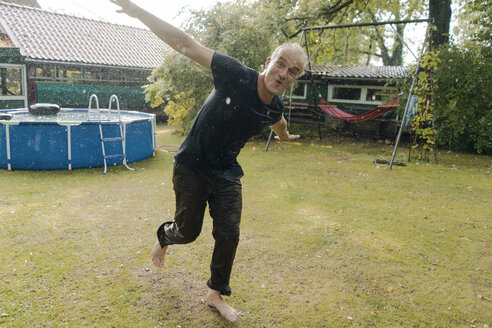 Portrait of carefree mature man enjoying summer rain in garden - KNSF04674