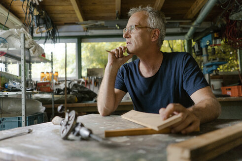Mature man at workbench in his workshop thinking - KNSF04693