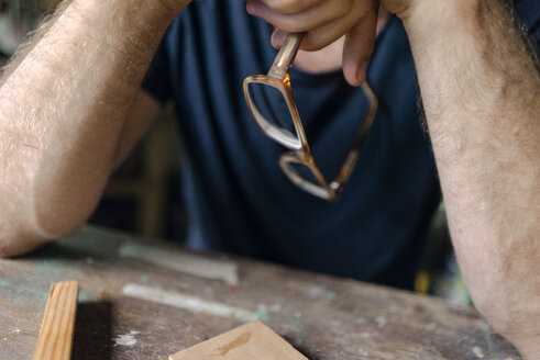 Close-up of man at workbench in workshop holding eyeglasses - KNSF04697
