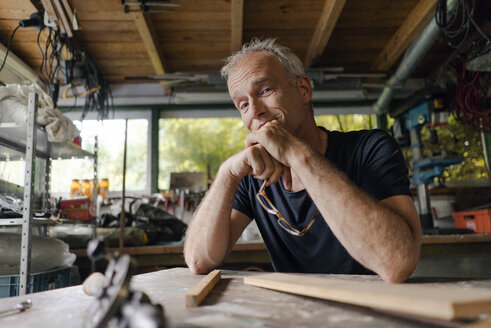 Portrait of confident mature man at workbench in his workshop - KNSF04698