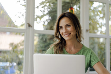 Smiling mature woman at the window with laptop - KNSF04713